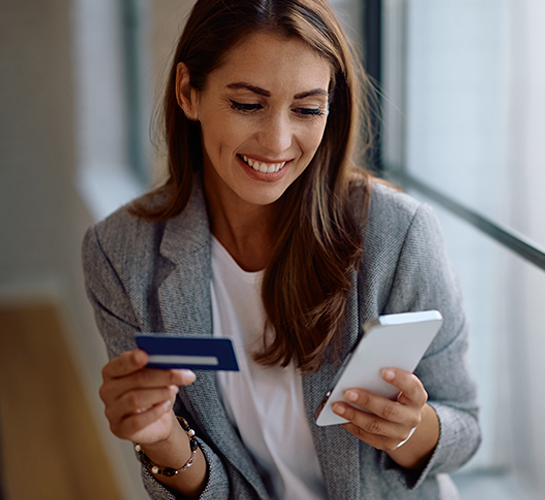 women smiling hold a phone in one hand and a card in the other