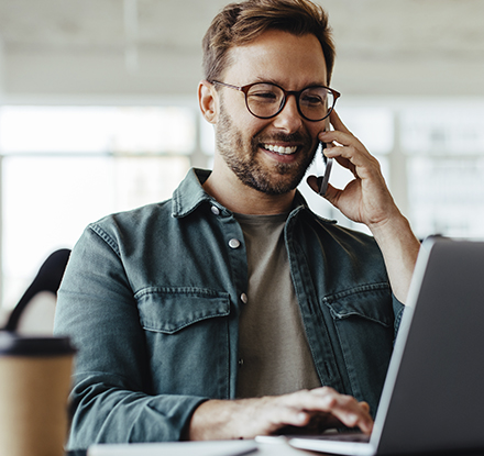 man smiling talking on phone looking at a laptop